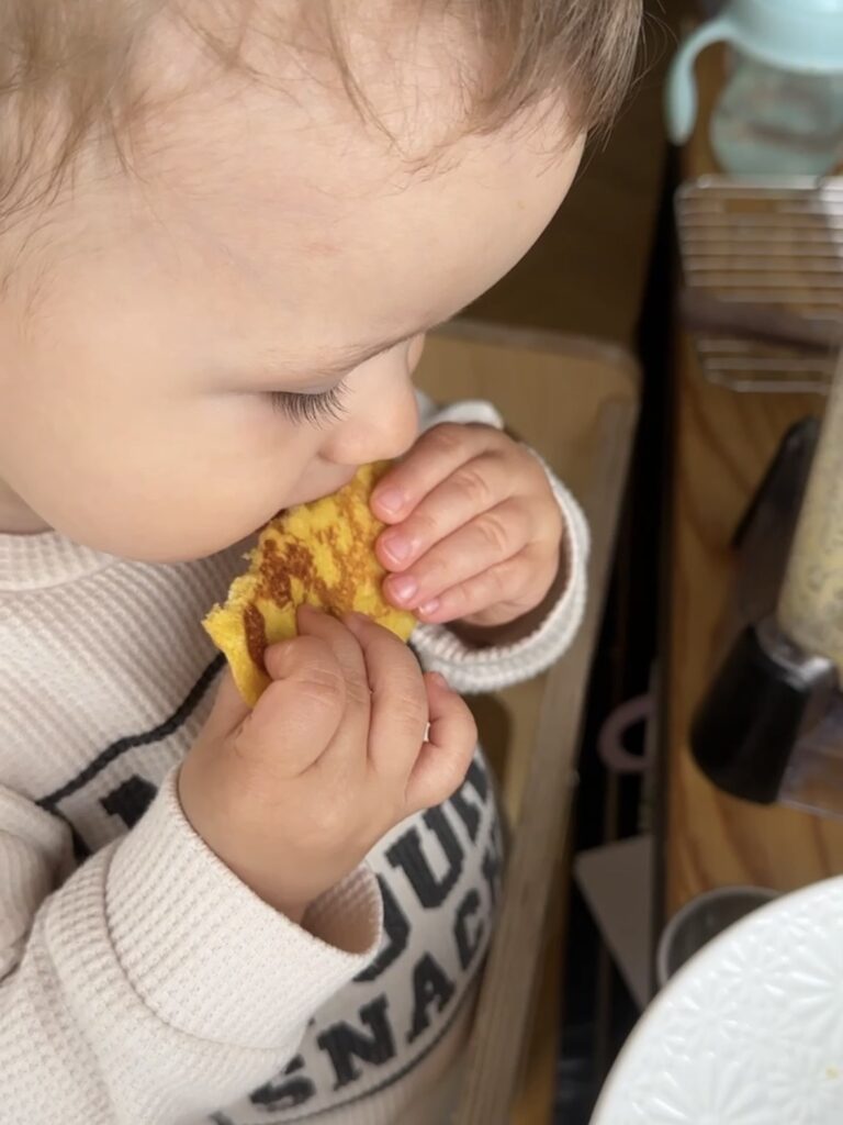 Bebé sosteniendo una cachapa pequeña con sus manos durante el desayuno
