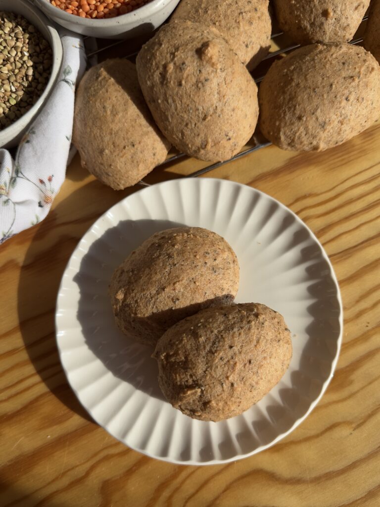 Pancitos de trigo sarraceno y lentejas rojas sin gluten en un plato blanco con bowls de ingredientes al fondo