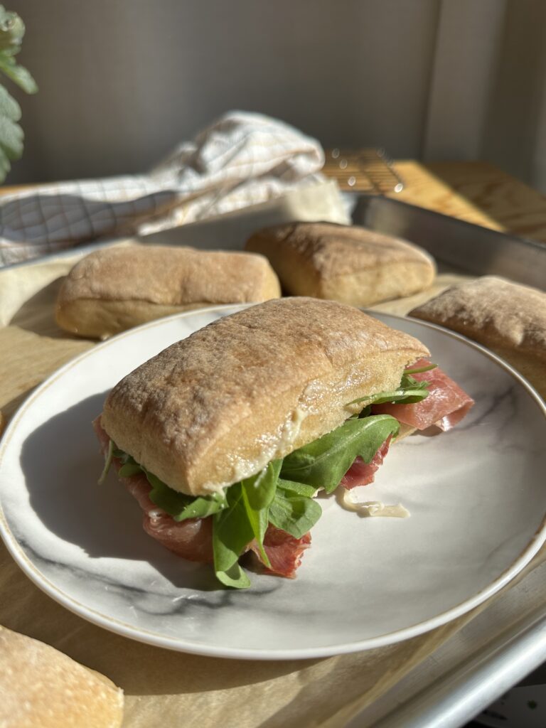 Bocadillo de ciabatta sin gluten relleno de jamón serrano y rúcula sobre plato de mármol