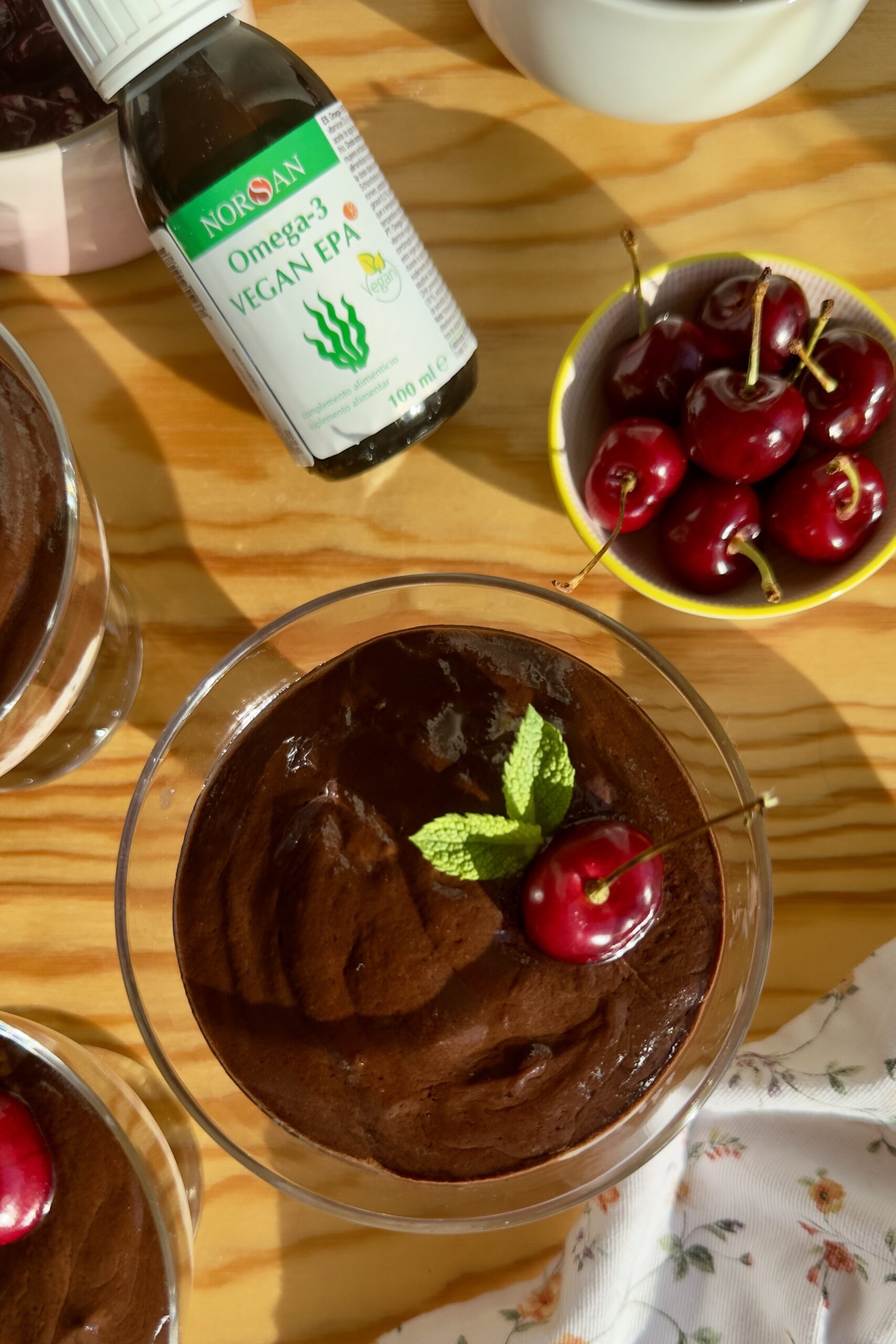 Vasito de pudding de chía con ganache de chocolate y cereza fresca junto a la botella de aceite Omega-3 Vegan EPA de NORSAN